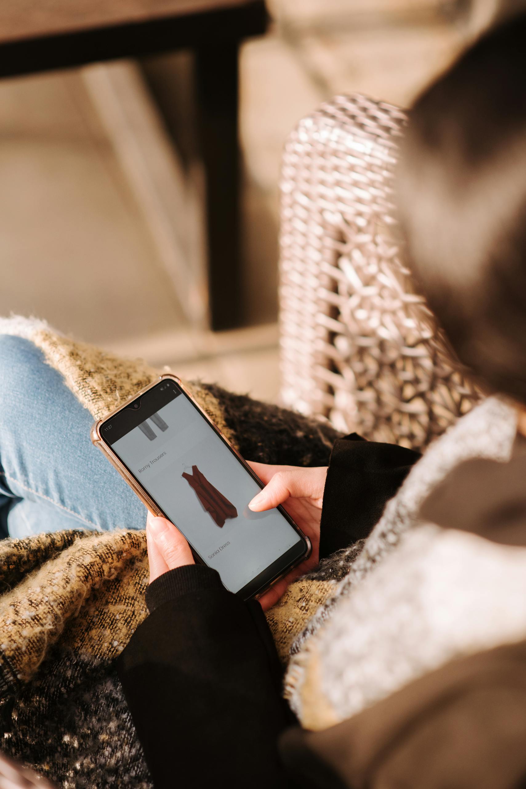 A woman comfortably browsing online shopping for a dress using her smartphone, enjoying leisure time indoors.